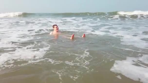 Όμορφος άντρας να πέφτει στο νερό. Ένας ενήλικας ξαπλωμένος στην ακτή του ωκεανού και τον πλένουν τα κύματα της θάλασσας.. — Αρχείο Βίντεο