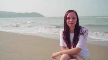 Yakışıklı kadın sahile yakın kumsalda duruyor. Deniz kıyısında güneşli bir günde gülümseyen kadın turist..
