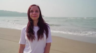 Yakışıklı kadın sahile yakın kumsalda duruyor. Deniz kıyısında güneşli bir günde gülümseyen kadın turist..