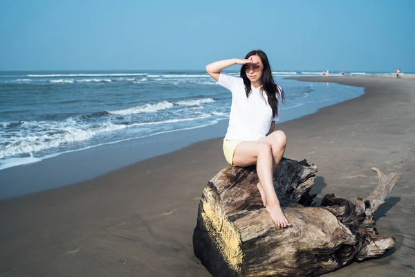 Mulher relaxada sentada no tronco e olhando para o outro lado. turista feminino descansando na praia de areia perto do mar ondulando. — Fotografia de Stock