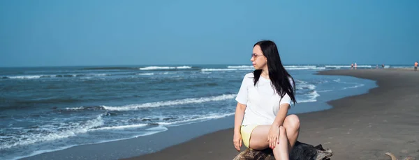 Mulher relaxada sentada no tronco e olhando para o outro lado. turista feminino descansando na praia de areia perto do mar ondulando. — Fotografia de Stock