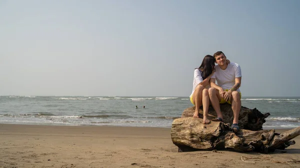 Casal feliz posando em troncos perto do mar. Amante casal abraçando durante a data na praia contra o mar ondulando e céu sem nuvens . — Fotografia de Stock