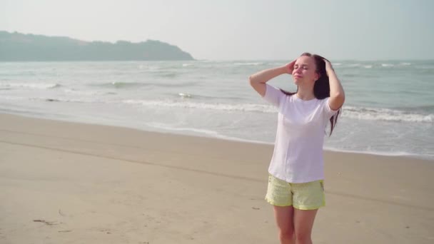 Entspannte Frau steht auf, richtet ihre Haare am Ufer. Porträt einer angenehmen Dame, die an sonnigen Tagen ihren Urlaub genießt und ihr langes Haar am Strand streichelt. — Stockvideo