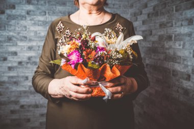 Crop elderly woman with flowers. Unrecognizable senior lady carrying wrapped bouquet of colorful flowers during holiday celebration