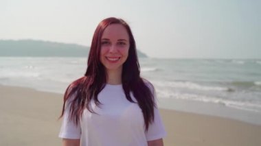 Yakışıklı kadın sahile yakın kumsalda duruyor. Deniz kıyısında güneşli bir günde gülümseyen kadın turist..