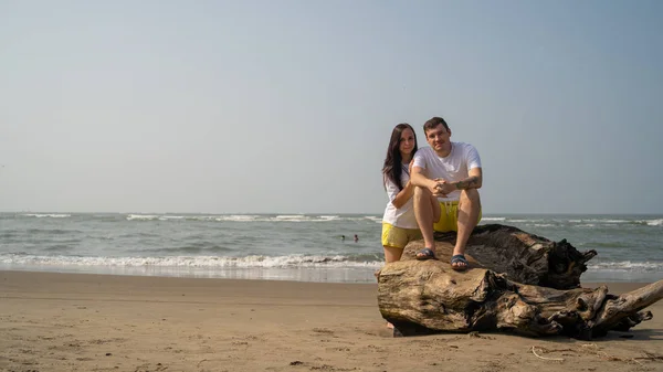 Casal feliz posando em troncos perto do mar. Amante casal abraçando durante a data na praia contra o mar ondulando e céu sem nuvens . — Fotografia de Stock