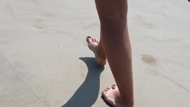 Female feet with red pedicure walking on sandy beach. Slow motion in close up. Female tourist spending time enjoying vacation and promenading on beach. — ストック動画