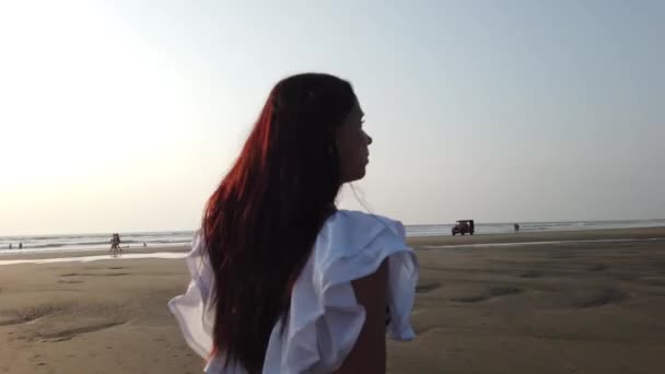 Relaxed woman walking along sea coast. Portrait of pleasant lady spending time enjoying vacation and promenading on seashore against sunset. — Stockvideo