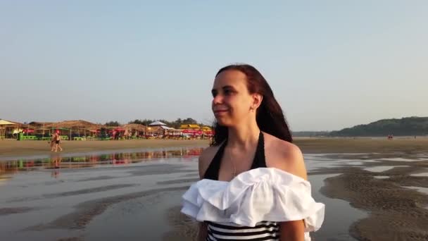 Relaxed woman walking along sea coast. Portrait of pleasant lady spending time enjoying vacation and promenading on seashore against sunset. — Stockvideo