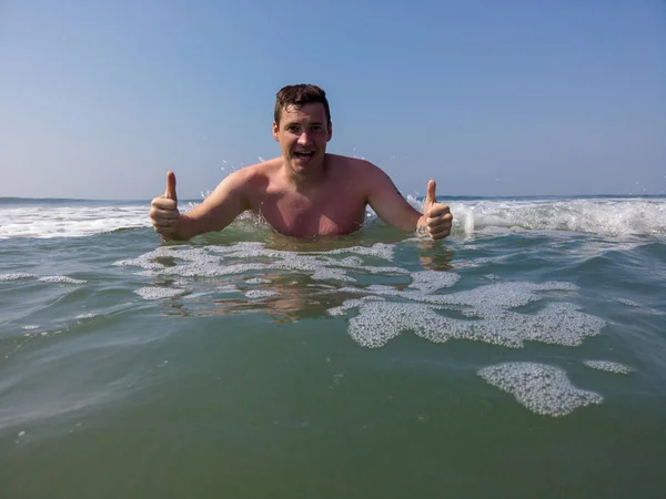 Férfi a tengerben a part közelében. Vonzó férfi a tengeren, vizet fröcsköl és pózol a kamerának. Mosolygó ember szórakozás tengervízben. — Stock Fotó
