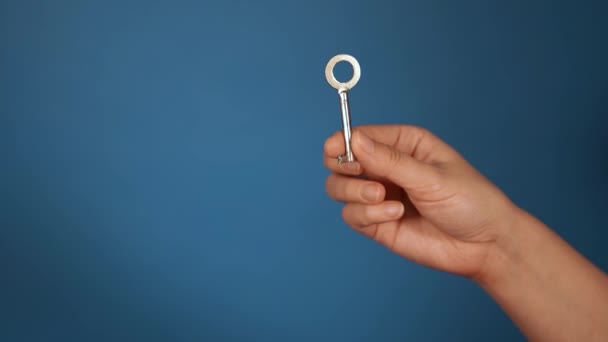 Primer plano de la mano con llave. Mano de mujer sosteniendo una tecla sobre fondo azul . — Vídeo de stock