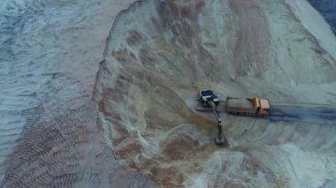 Kazıcı, toprağı nakliye kamyonuna yüklüyor. Ağır bir makine, kazıcı ve kamyon kum ocağında çalışıyor..