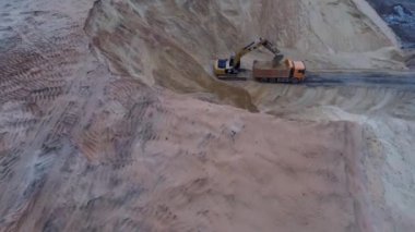 Kazıcı, toprağı nakliye kamyonuna yüklüyor. Ağır bir makine, kazıcı ve kamyon kum ocağında çalışıyor..