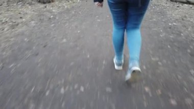 Kot pantolon ve spor ayakkabı giymiş bir kız ormanda yürüyor, ayaklarının üzerinde. Bir dişi turist dar bir orman yolu boyunca yürür. Yakın bacaklar, yolda yürüyen bir kız.