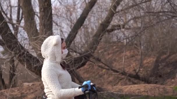 Молодая женщина в медицинской маске и перчатках стоит с велосипедом, держа руль в сельской местности. Женщина защищает себя от болезней во время ходьбы. Концепция угрозы коронавирусной эпидемии . — стоковое видео