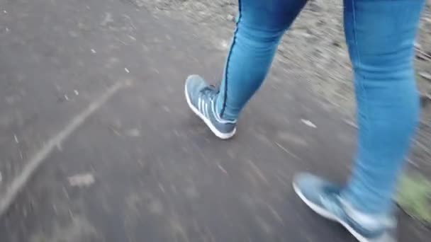 En flicka klädd i blå jeans och gympaskor går genom skogen, närbild på fötterna. En kvinnlig turist går längs en smal skogsstig. Närbild ben, en flicka går, går längs stigen — Stockvideo