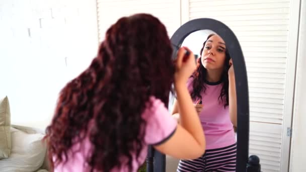 Jonge mooie vrouw in pyjama schildert haar wimpers van mascara, kijkend in spiegel thuis. close-up van charmante vrouwelijke preening voor grote spiegel, make-up. — Stockvideo