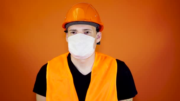 Retrato de un joven con máscara médica en su cara sobre fondo naranja. Masculino adulto cubierto la cara con máscara para protegerse de enfermedades. Concepto de epidemia o enfermedades por coronavirus . — Vídeo de stock