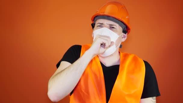 Hombre trabajador de la construcción en overoles y máscara médica tosiendo sobre fondo naranja. Concepto de amenaza de infección . — Vídeo de stock