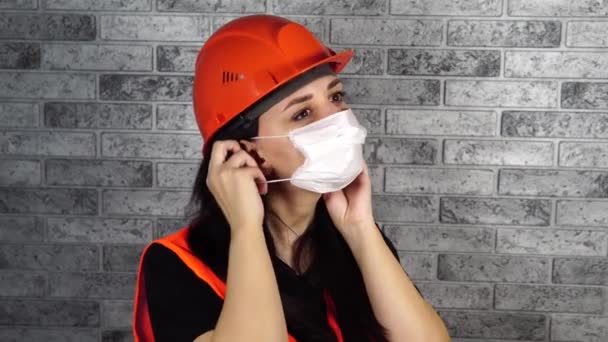 Female construction worker in overalls putting on medical mask on face on background of gray brick wall — Stock Video