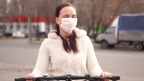 의료용 마스크를 쓴 젊은 여성 이 도시의 거리에서 자전거를 들고 서 있습니다. 성인 여성은 걷는 도중의 질병으로부터 자신을 보호하기 위해 마스크로 얼굴을 가렸다. 코로나 바이러스 의유 행병 감염의 위협에 대한 개념. — 비디오