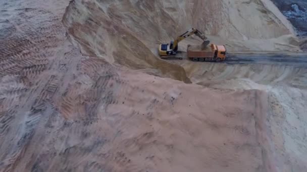 Excavator loading soil onto hauler Truck, Top down aerial footage. A heavy machinery - excavator and truck are working in the sand quarry. — Stock Video