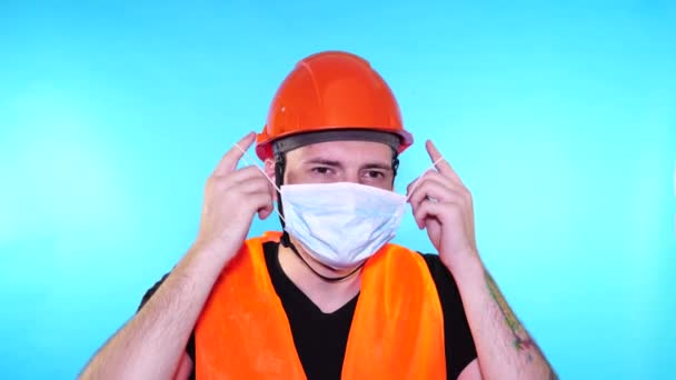 Muž stavební dělník v montérkách odstranění lékařské masky z obličeje na modrém pozadí. — Stock video