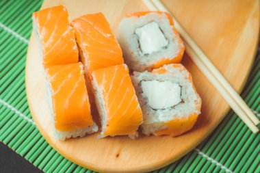 Dekoratif bambu peçetede ahşap tahtanın üzerinde nefis rulo. Lezzetli suşi rulolarını kesme tahtasının üzerinde çubuklarla kapatın..