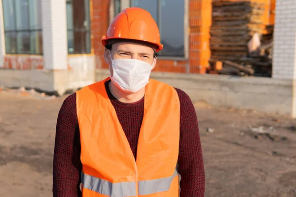 Портрет строителя-мужчины в медицинской маске и комбинезоне на фоне строящегося дома . — стоковое фото