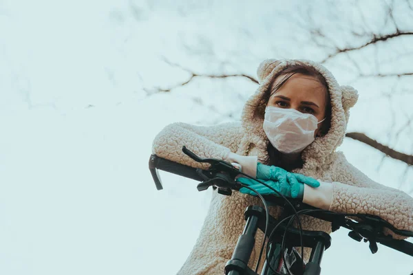 Портрет молодой женщины в медицинской маске и перчатках с велосипедом против неба. Взрослая женщина покрывает лицо, чтобы защитить себя от болезней во время ходьбы. Концепция угрозы коронавирусной эпидемии . — стоковое фото
