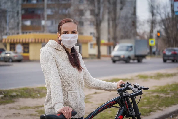 Молодая женщина в медицинской маске стоит с велосипедом на городской улице. Взрослая женщина покрывает лицо маской, чтобы защитить себя от болезней во время ходьбы. Концепция угрозы коронавирусной эпидемии . — стоковое фото