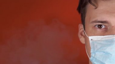 Yüzünde tıbbi maske olan bir adam. Kameraya bakan erkek yüzünün yakın çekimi. Yetişkin adam yüzünü dumandan maskeyle örttü. Sigara karşıtı kavram.