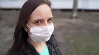 Sokakta duran tıbbi maske takmış genç bir kadının portresi. Yetişkin kadın kendini hastalıklardan korumak için yüzünü maskeyle örttü..