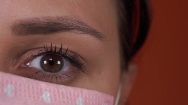 Turuncu bir arka planda yüzünde tıbbi maskesi olan bir kadın. Coronavirüs Salgını.