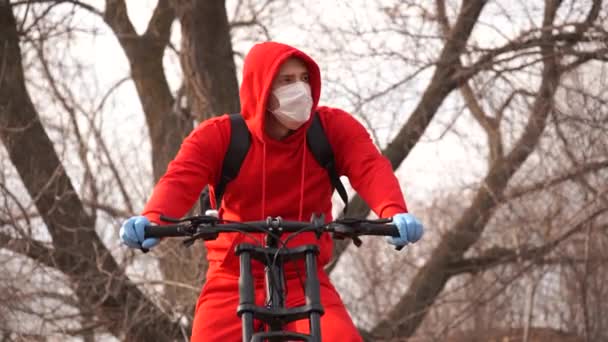 Ung man i medicinsk mask och handskar hosta på landsbygden. Vuxen man i röd kostym skyddar dig från sjukdomar på promenad. Begreppet hot om infektion med coronavirus. — Stockvideo