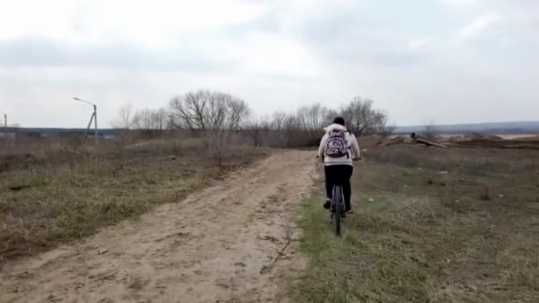 Mujer joven montando bicicleta en el campo. Mujer adulta en ropa casual con mochila disfrutando de la naturaleza mientras monta en bicicleta. Concepto de estilo de vida saludable . — Vídeo de stock