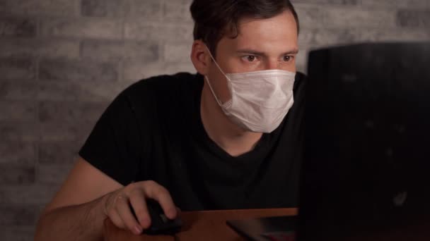 Człowiek w masce medycznej dowiaduje się o wirusie z Internetu za pomocą laptopa. Mężczyzna martwi się o swoje zdrowie. Epidemia koronawirusa. — Wideo stockowe