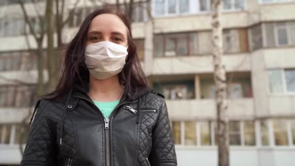 通りに立っている彼女の顔に医療用マスクの若い女性の肖像画。大人の女性は病気から身を守るためにマスクで顔を覆いました. — ストック動画