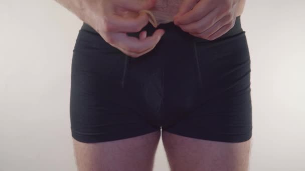 Close-up de um homem de cueca segurando um preservativo em um fundo branco. Homem de cuecas a segurar um preservativo e um contraceptivo. Contracepção - homem de roupa interior — Vídeo de Stock