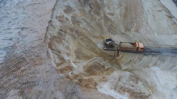 Excavadora cargando tierra sobre camión de transporte, imágenes aéreas de arriba hacia abajo. Una maquinaria pesada excavadora y camión están trabajando en la cantera de arena . — Vídeos de Stock