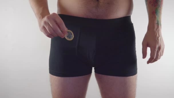 Close-up van een man in ondergoed met een condoom op een witte achtergrond. Een man in ondergoed met een condoom en een anticonceptiemiddel. Anticonceptie - man in ondergoed — Stockvideo