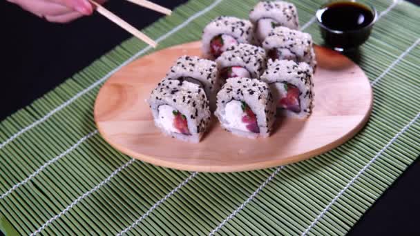 Comer rollos de sushi con palillos. Comida japonesa en el restaurante. La mujer sostiene sushi con palillos. Concepto de comida japonesa . — Vídeos de Stock
