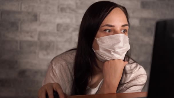 A woman in a medical mask learns news about the coronavirus from the Internet using a laptop. Female is concerned about his health. The Epidemic Of Coronavirus. — Stock Video