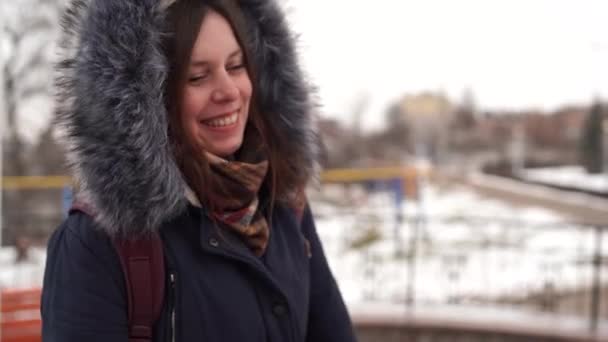 Portret van een jonge vrouw, lachend op het platteland in het winterseizoen. Volwassen vrouw in capuchon jas knabbelen in gesprek met iemand. — Stockvideo