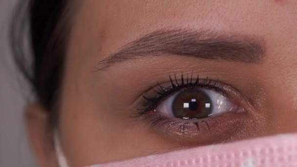 En kvinna med en medicinsk mask på ansiktet på en grå bakgrund. Coronavirusets epidemi. — Stockvideo