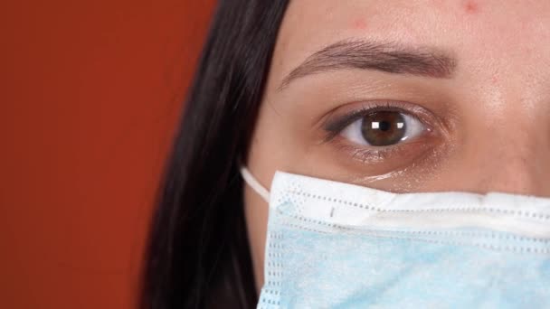 Turuncu bir arka planda yüzünde tıbbi maskesi olan bir kadın. Coronavirüs Salgını. — Stok video