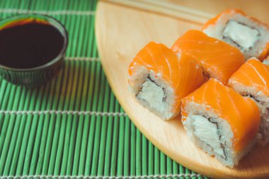 Süslü bambu peçetesinde soya soslu ahşap tahta rulo. Lezzetli suşi rulolarını siyah arka planda kesme tahtasıyla kapatın..