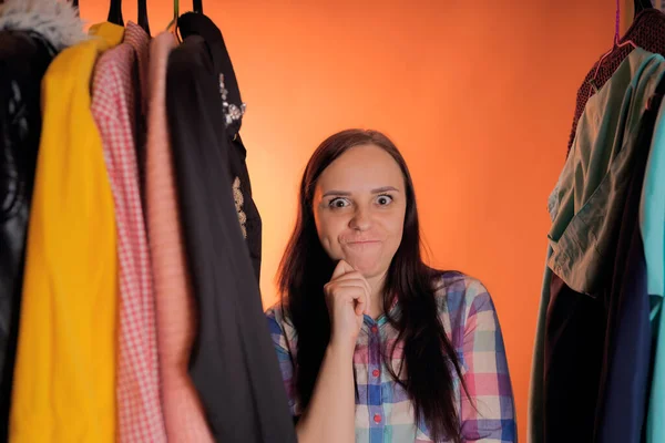 Jonge vrouw grimmig staande tussen kleren in de kast. Volwassen vrouw die dingen in petto heeft. — Stockfoto