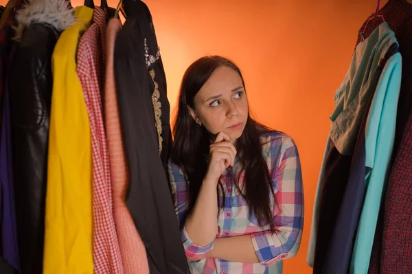 Jonge vrouw grimmig staande tussen kleren in de kast. Volwassen vrouw die dingen in petto heeft. — Stockfoto