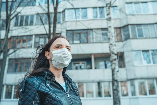 Portrait of young woman in medical mask on her face standing on street. Adult female covered her face with mask to protect yourself from diseases.